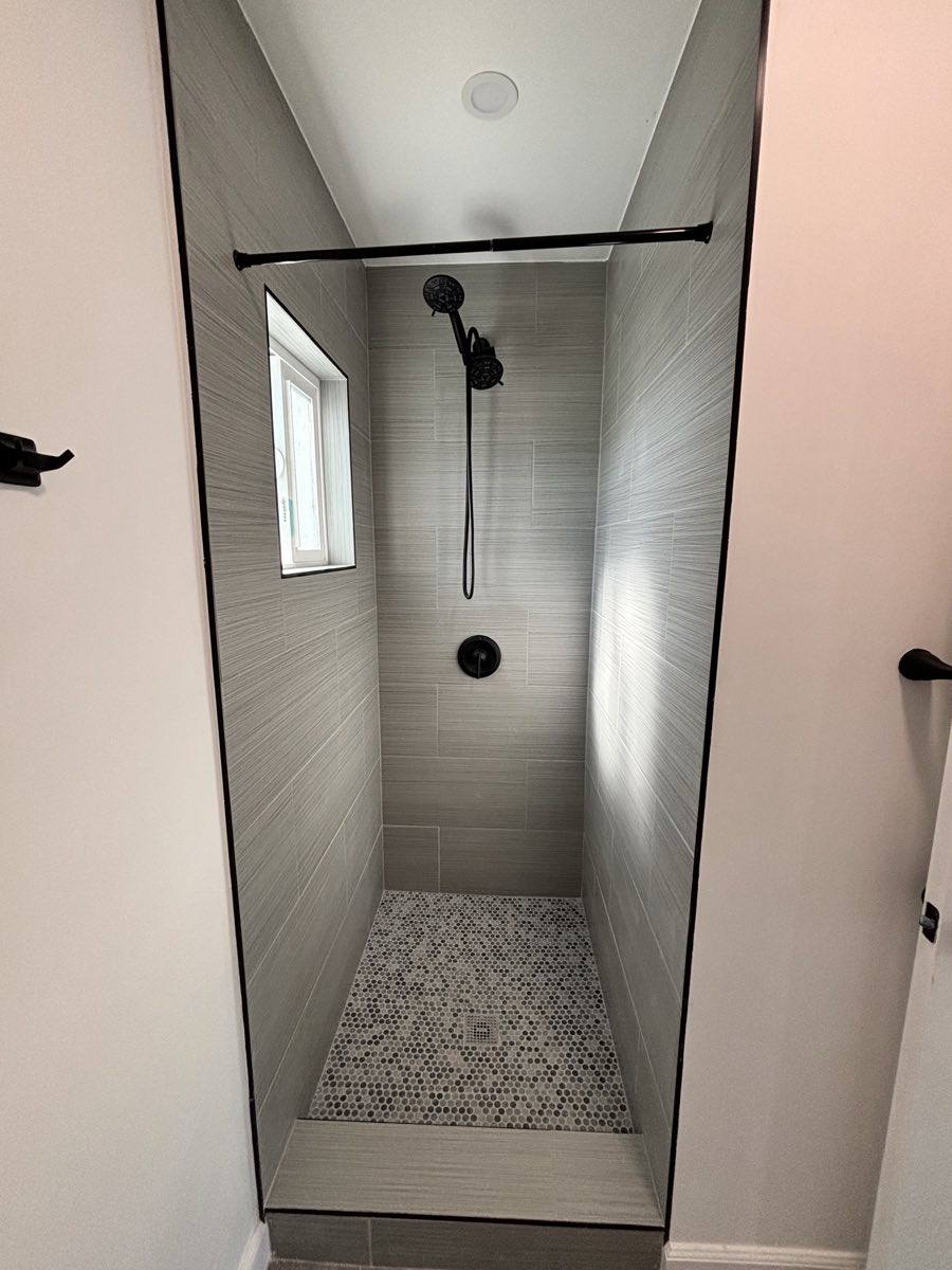 Grey tile walk in shower with penny round floor and black fixtures